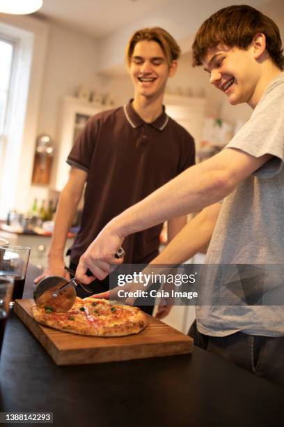 happy teenage boys slicing fresh pizza in kitchen - making pizza stock pictures, royalty-free photos & images