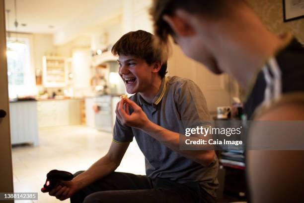 happy teenage boy playing video game and eating at home - friends laughing at iphone video stock pictures, royalty-free photos & images