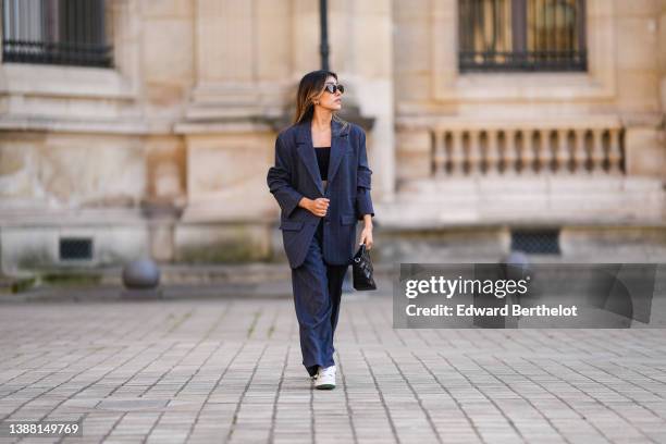 Angela Gonzalez wears black sunglasses, gold and silver earrings, a navy blue striped print pattern oversized blazer jacket, matching navy blue...