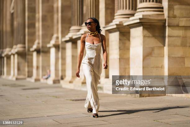 Emilie Joseph @in_fashionwetrust wears black sunglasses, earrings, an oversized gold chain necklace from JW Anderson, a beige linen square neck /...