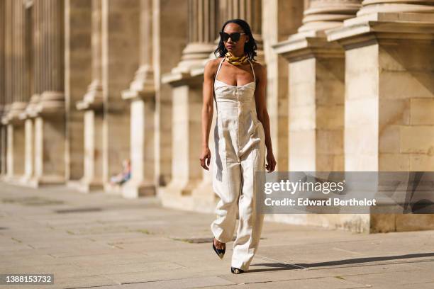 Emilie Joseph @in_fashionwetrust wears black sunglasses, earrings, an oversized gold chain necklace from JW Anderson, a beige linen square neck /...