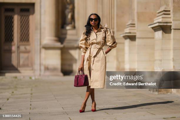 Emilie Joseph @in_fashionwetrust wears black sunglasses, a beige ruffled puffy shoulder / belted long coat worn as a dress from Magalie Pascal , a...