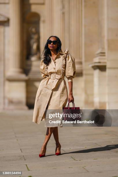 Emilie Joseph @in_fashionwetrust wears black sunglasses, a beige ruffled puffy shoulder / belted long coat worn as a dress from Magalie Pascal , a...