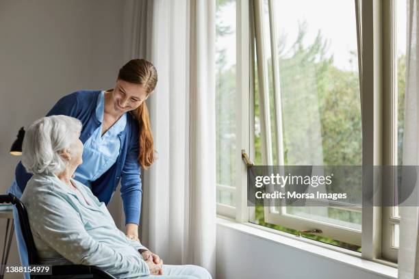 caregiver talking with woman sitting on wheelchair - pflegedienst blau stock-fotos und bilder