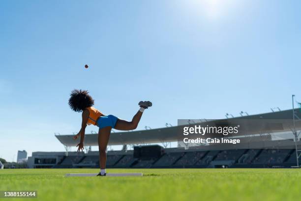 female track and field athlete throwing shot put in sunny stadium - kugelstoßen stock-fotos und bilder