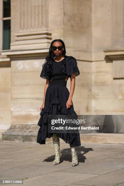 Emilie Joseph @in_fashionwetrust wears black sunglasses, a black ruffled puffy short sleeves / cut-out waist / asymmetric midi dress from Magalie...
