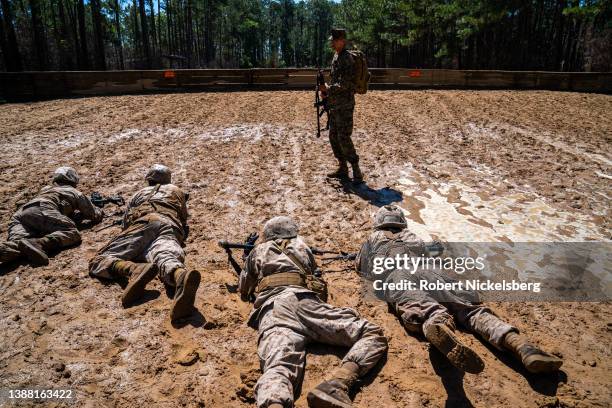 Marine Corps drill instructor watches as Marine recruits crawl through mud as they go through a simulated resupply effort during a Crucible training...