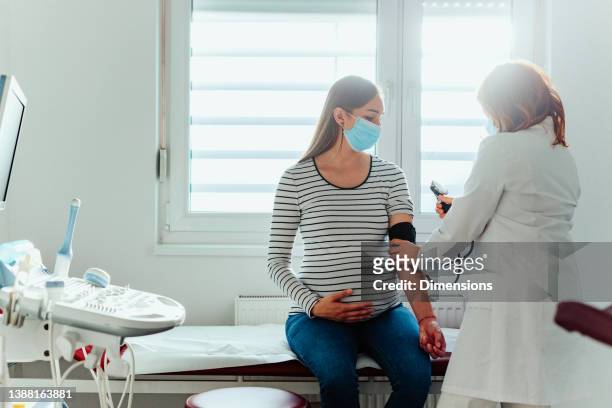 schwangere frau bei untersuchung in arztes praxis während pandemie - pregnant woman at doctor stock-fotos und bilder