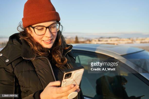 young woman texting outside by her car in winter - sunny winter stock pictures, royalty-free photos & images