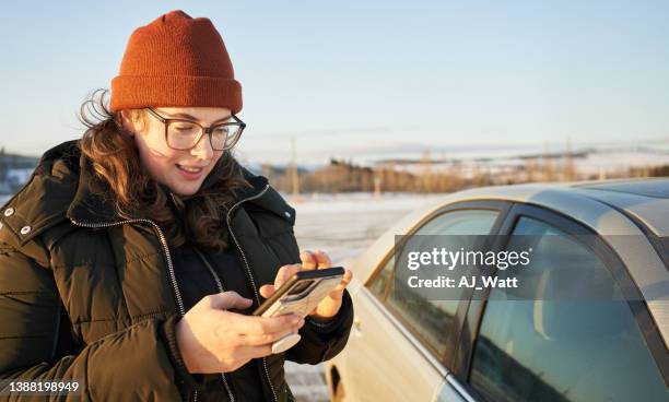 junge frau schreibt im winter an ihrem handy neben ihrem auto sms - winter panne auto stock-fotos und bilder