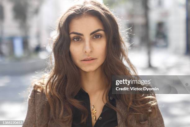 stylish model dressed in a brown coat and a black shirt looks curiously at the camera. - woman long brown hair stock pictures, royalty-free photos & images