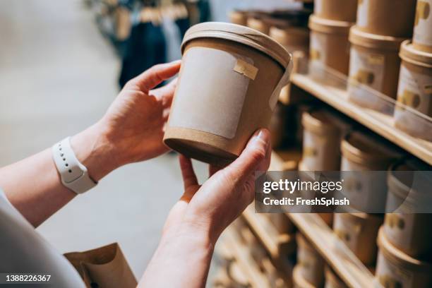 un gros plan d’une femme méconnaissable dans un magasin tenant un emballage biodégradable d’un produit décidant de l’acheter ou non - biodegradable photos et images de collection