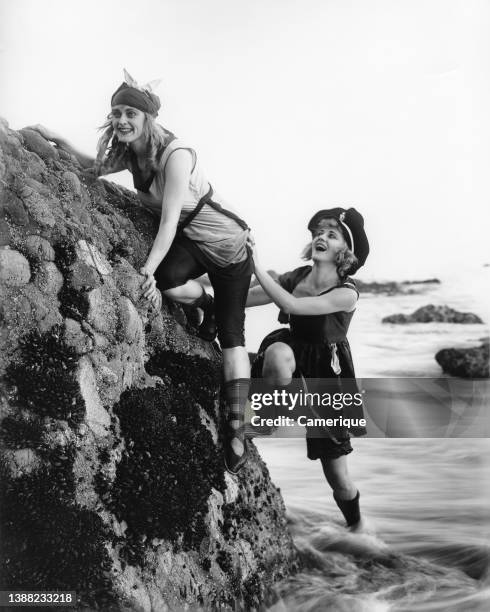Two women in 1920's attire on the beach climbing on the rocks at the beach. Circa 1920