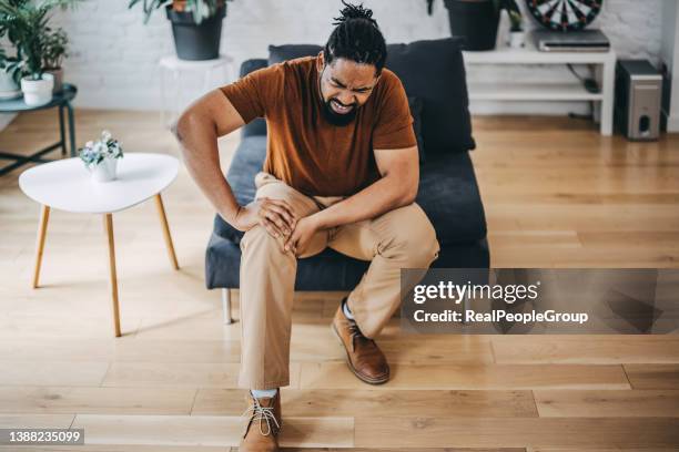 mid adult man suffering from knee pain sitting sofa - cartilage bildbanksfoton och bilder