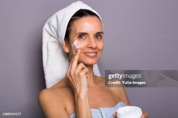 close-up of mature woman applying cream against gray background - smiling woman on gray background 50 stock pictures, royalty-free photos & images