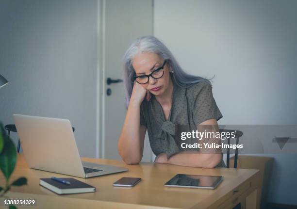 tired mature woman sitting at desk - autonomo smartphone tablet fotografías e imágenes de stock