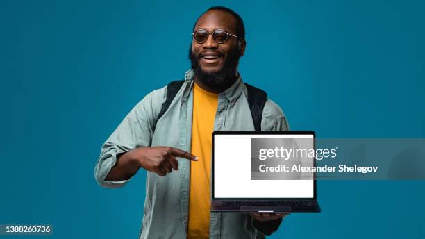 portrait african-american man at the studio with colored blue background. black person is showing empty screen of device for template and copy space concept. people with laptop computer - tonen stockfoto's en -beelden