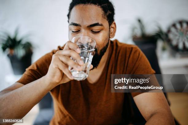 schwarzer mann, der zu hause ein glas wasser trinkt - wasserglas stock-fotos und bilder