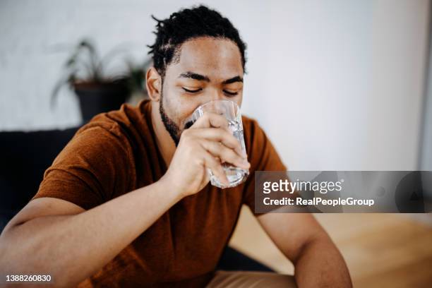 hombre negro bebiendo un vaso de agua en casa - man drinking water fotografías e imágenes de stock