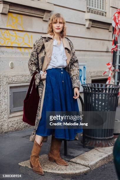 Latvian model Aivita Mūze wears a tan and black tiger print trench coat, white lace shirt, blue denim pleated skirt, brown suede cowboy boots, and a...