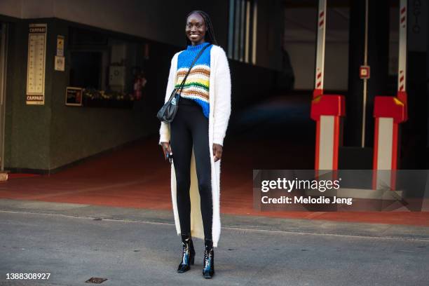 South Sudanese model Nyagua Ruea wears a long white cardigan jacket, blue striped knit top, small black Telfar bag, black leggings, black latex...