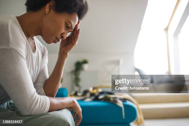 sad woman sitting with head in hand, looking down, battling anxiety - struggle stock pictures, royalty-free photos & images