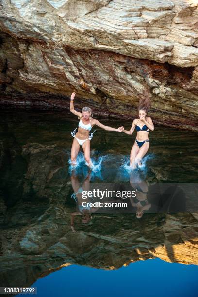 two young women in bikinis holding hands and diving into sea water with splash - cliff dive stock pictures, royalty-free photos & images