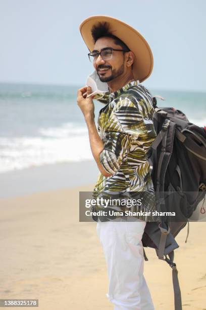 young man enjoying vacation on beach using phone while holding champagne glass in hand. - sand art in india stock-fotos und bilder