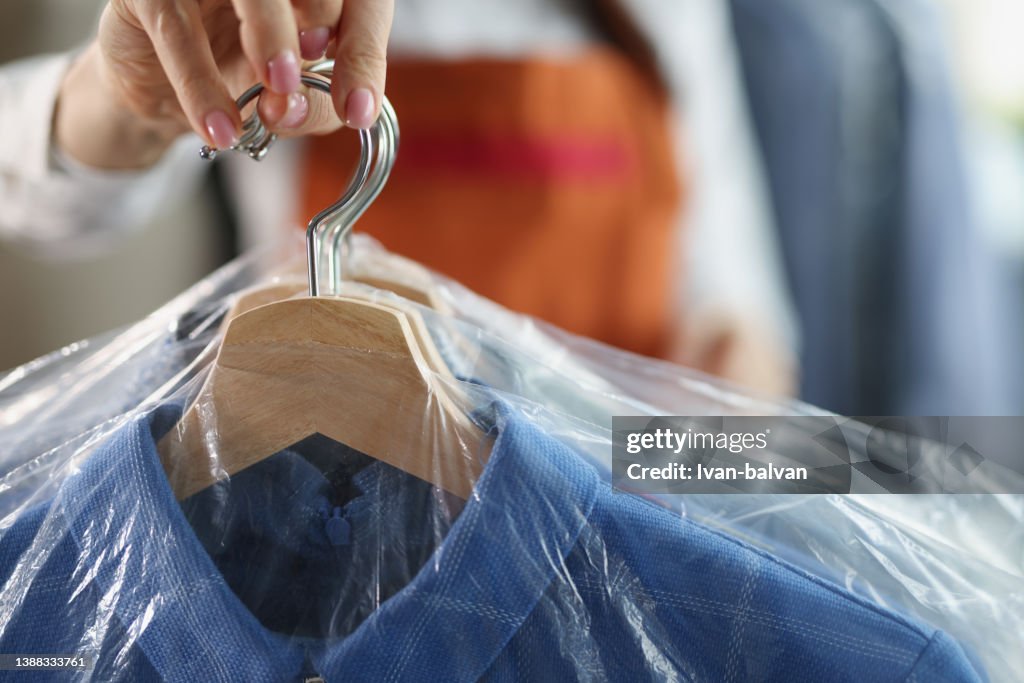 Worker giving to client clean clothes hanging on hangers at dry cleaning company