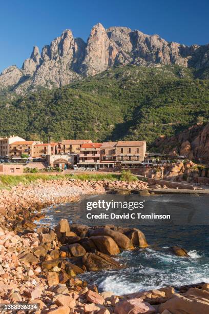 view across rocky cove to the village, buildings dwarfed by the steep rugged cliffs of capo d'orto, aka capu d'ortu, porto, corse-du-sud, corsica, france - corse du sud fotografías e imágenes de stock