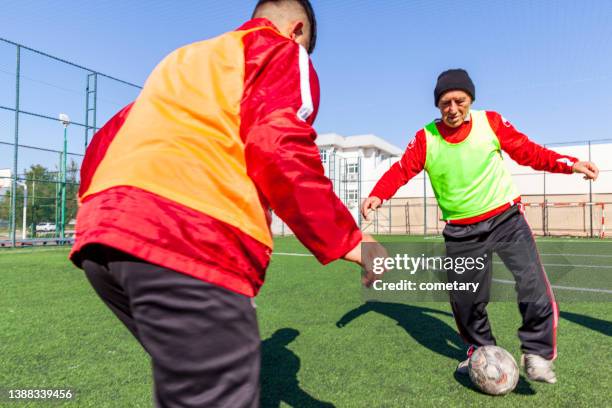 young men and senior men playing football - senior kicking stock pictures, royalty-free photos & images