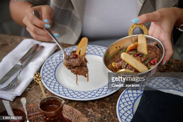 pouring spoonful of meat stew with flat bread slices in plate at the table in ethnic restaurant - vleesgerecht stockfoto's en -beelden