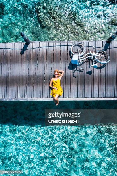 schöne frau, die auf dem steg mit fahrrad auf den malediven liegt - fahrradausflug stock-fotos und bilder