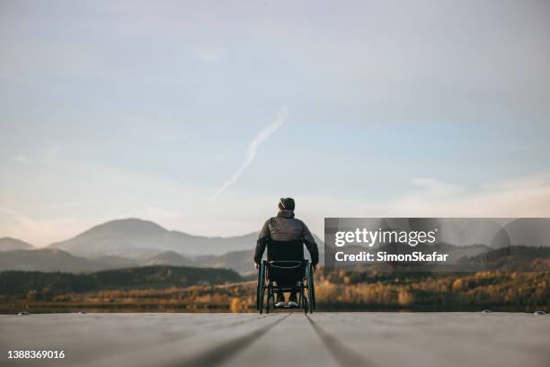 paraplegico in sedia a rotelle sul molo al tramonto - sedia a rotelle foto e immagini stock