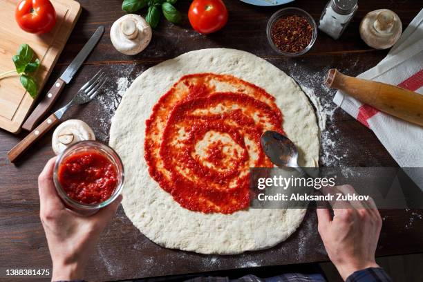 cooking italian vegetarian pizza with vegetables and mushrooms at home, pizzeria or cafe. a woman baker, pastry chef or cook spreads ketchup with a spoon on the dough, in a bakery. the concept of food. step-by-step instructions, do it yourself. step 1. - tomato paste stock pictures, royalty-free photos & images