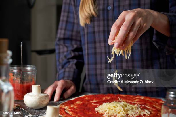 cooking italian vegetarian pizza with vegetables and mushrooms at home, pizzeria, bakery or cafe. a woman baker, pastry chef or cook puts and adds grated cheese. food concept. step-by-step instructions, do it yourself. step 1. - grated cheese stock pictures, royalty-free photos & images