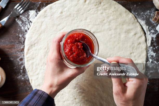 cooking italian vegetarian pizza with vegetables and mushrooms at home, pizzeria or cafe. a woman baker, pastry chef or cook spreads ketchup with a spoon on the dough, in a bakery. the concept of food. step-by-step instructions, do it yourself. step 1. - tomato paste stock pictures, royalty-free photos & images