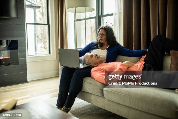 senior woman using laptop on couch while husband naps - healthy older couple stock pictures, royalty-free photos & images