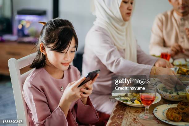 young malay girl using smartphone while having hari raya family reunion dinner - dinner program stock pictures, royalty-free photos & images