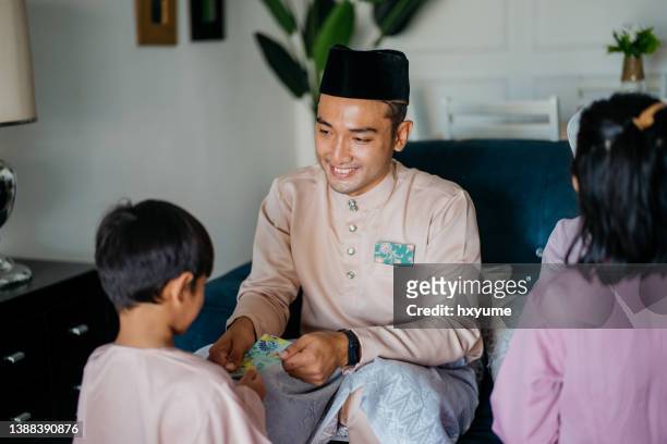malay muslim parents in traditional clothings giving gift of money to their children during hari raya aidilfitri celebration - ramadan giving stockfoto's en -beelden
