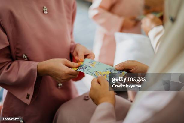 malay muslim parents in traditional clothings giving gift of money to their children during hari raya aidilfitri celebration - ramadan giving stockfoto's en -beelden