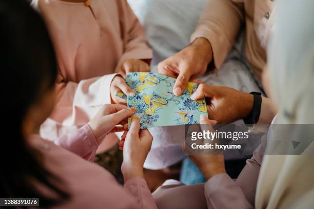 malay muslim parents in traditional clothings giving gift of money to their children during hari raya aidilfitri celebration - mom blessing son stockfoto's en -beelden