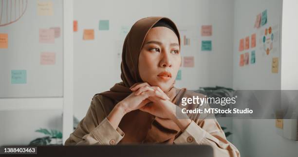 joven empresaria musulmana asiática frustrada que usa hiyab trabajando en una computadora portátil sentada en el escritorio de la oficina. - distressed stock market people fotografías e imágenes de stock