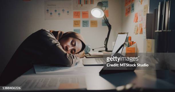 exhausted young asian muslim  businesswoman wearing hijab hard work sleeping while sitting at desk in office at night. - a hard days night imagens e fotografias de stock