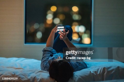 Woman lying down on bed and using smart phone at night Woman lying down on bed and using smart phone at night