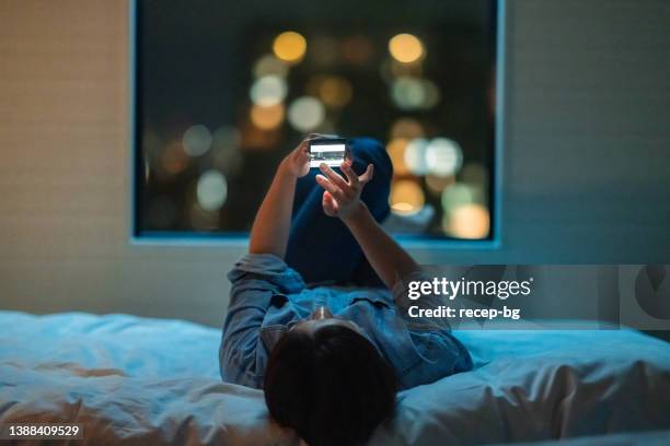 woman lying down on bed and using smart phone at night - good night imagens e fotografias de stock