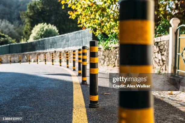 line of road bollards on curved road in sunlight. - bollards fotografías e imágenes de stock