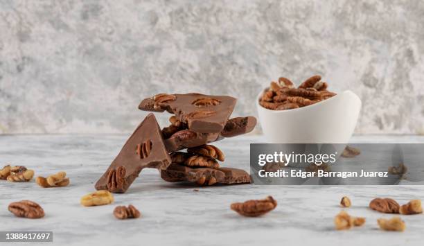 chunk chocolate bar with a bowl of pecans next to it on a gray granite table - caramel block stock pictures, royalty-free photos & images