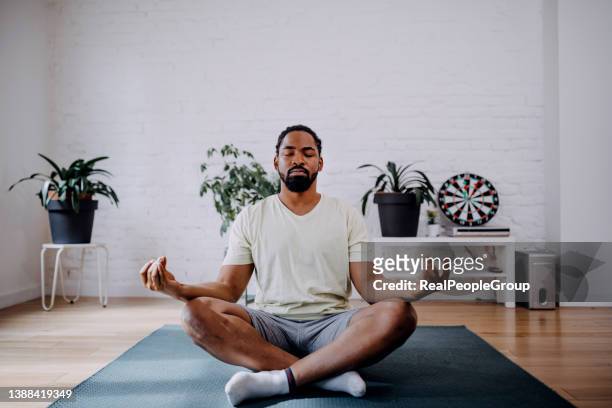 concepto de acondicionamiento físico, meditación y estilo de vida saludable: hombre negro meditando en pose de loto en una esterilla de ejercicio en casa - buddhism fotografías e imágenes de stock