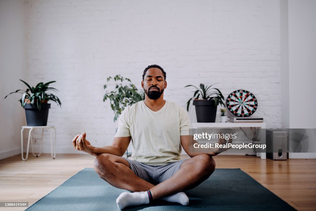 Fitness, méditation et concept de mode de vie sain - homme noir méditant en lotus pose sur un tapis d’exercice à la maison